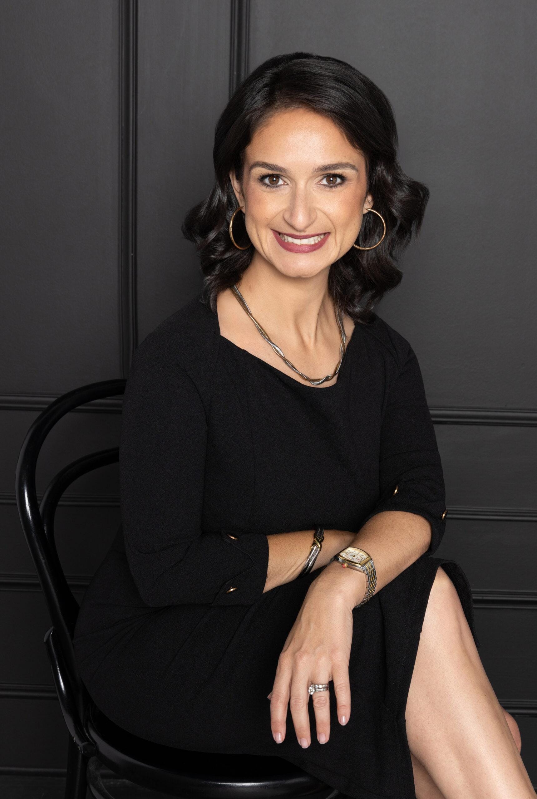 Christina Vilaboa-Abel, bankruptcy and insolvency attorney at CAVA Law, seated in a black dress, smiling confidently against a dark backdrop, highlighting her professional demeanor.